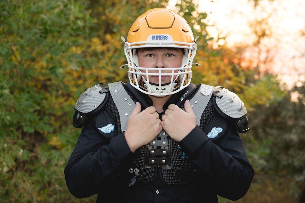 Young football player in gold Miners helmet and shoulder pads posing outdoors in fall foliage. Travel Photographer