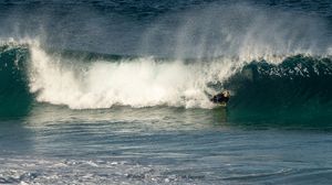 Surfer riding inside a massive crashing ocean wave barrel in clear blue water.