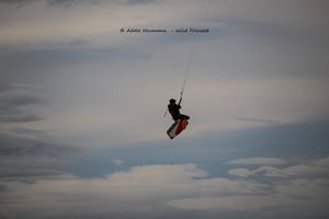 A kitesurfer soars high in the air against a cloudy sky, performing an impressive aerial trick while kiteboarding.