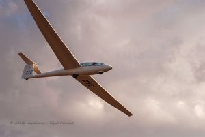 A white glider soaring gracefully through a dramatic cloudy sky at dusk, with long slender wings.