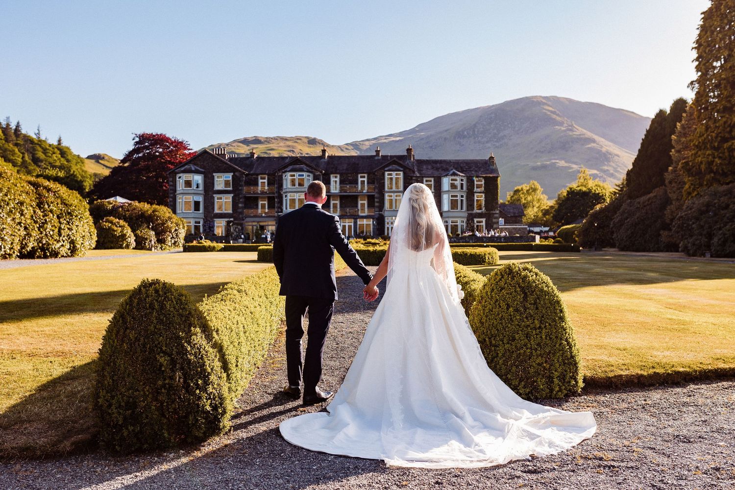 A bride and groom walk hand in hand toward their reception at Inn on the Lake