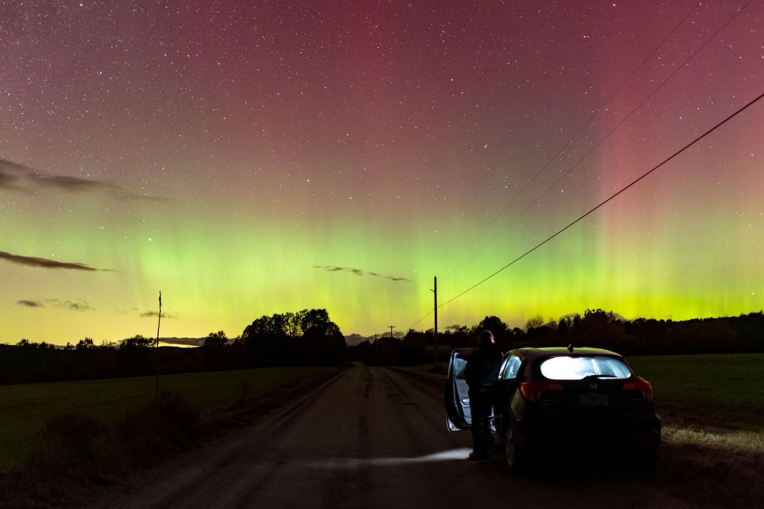 Stunning aurora borealis with green and red lights illuminating night sky over rural road with car.
