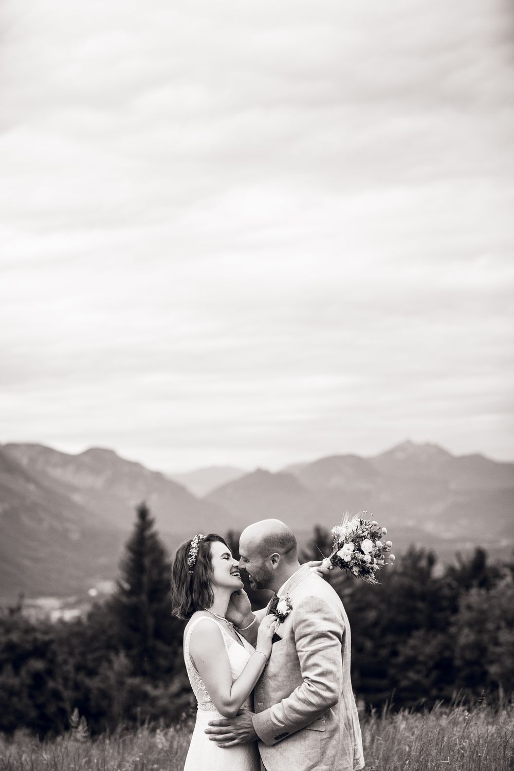 Black and white photo of a bride and groom embracing and about to kiss with mountain scenery behind them.