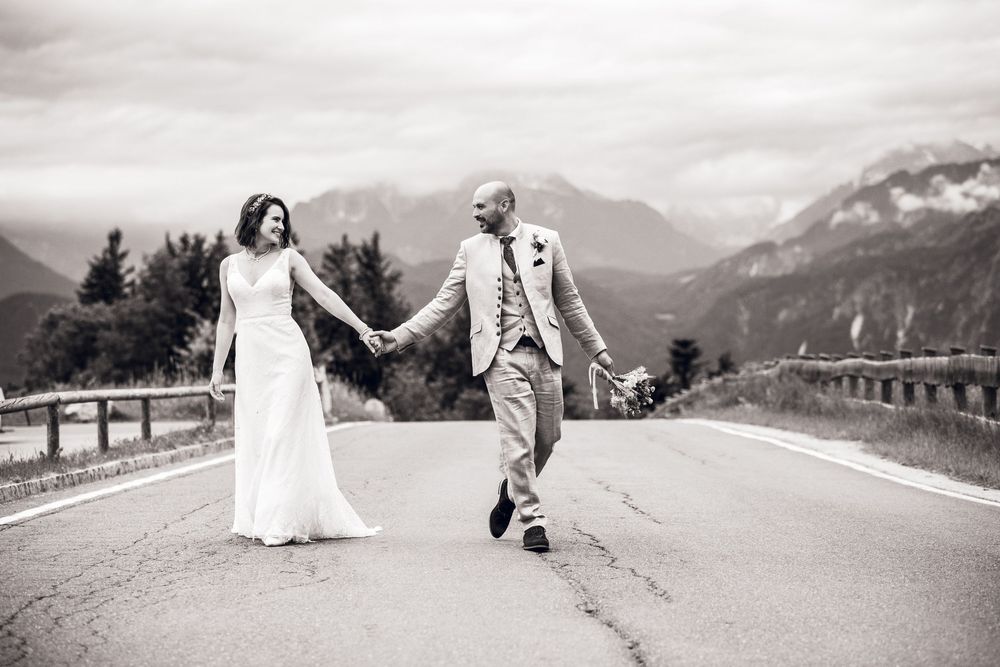 Black and white photo of bride and groom holding hands walking on mountain road on their wedding day.