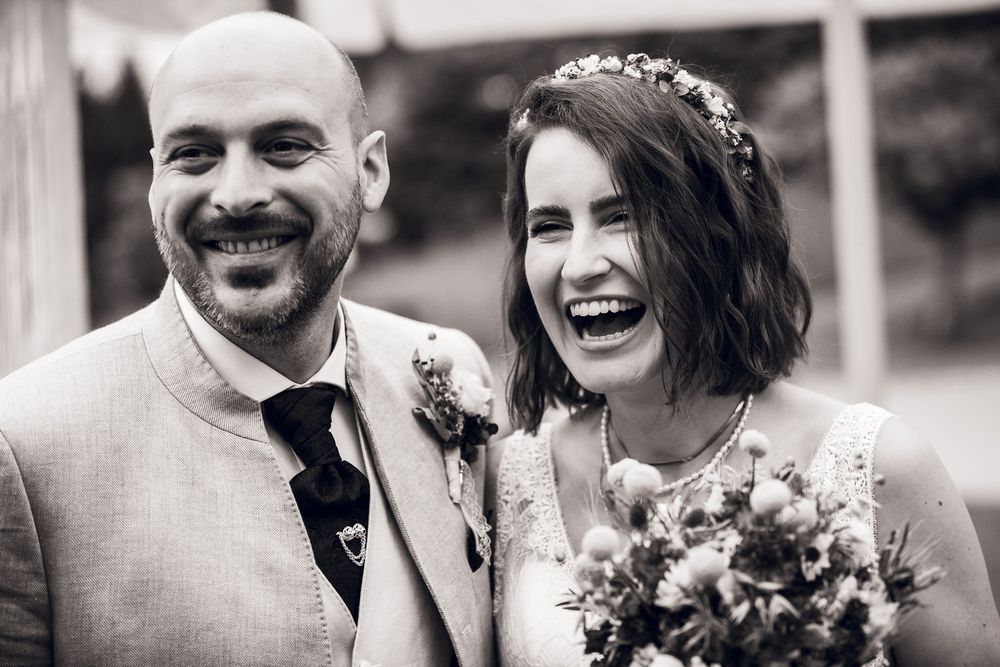 Laughing bride and groom share joyful moment in close-up black and white wedding photo.