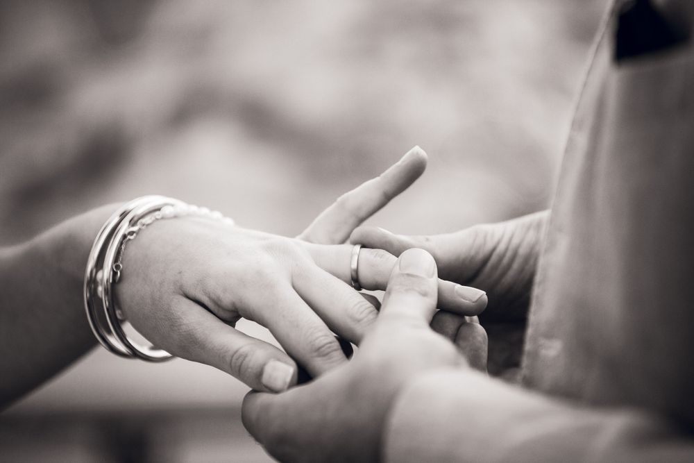 Close-up black and white photo of groom placing wedding ring on brides finger during ceremony.