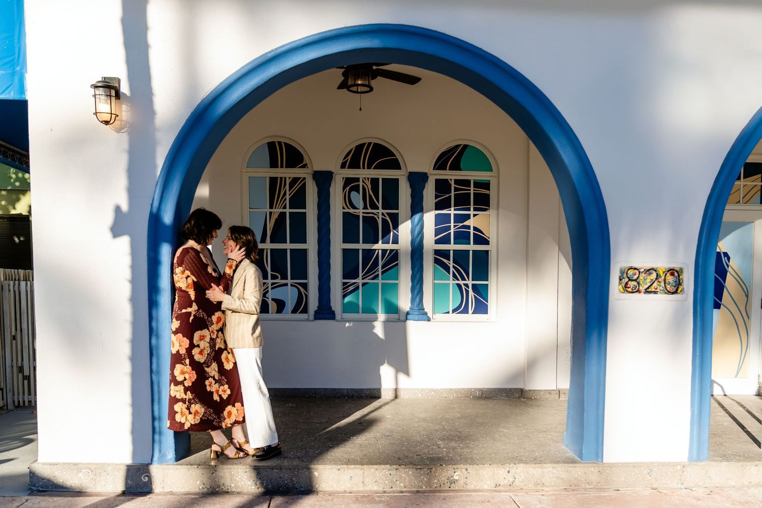 Couple embracing under a blue and white arched doorway of a Mediterranean-style building.