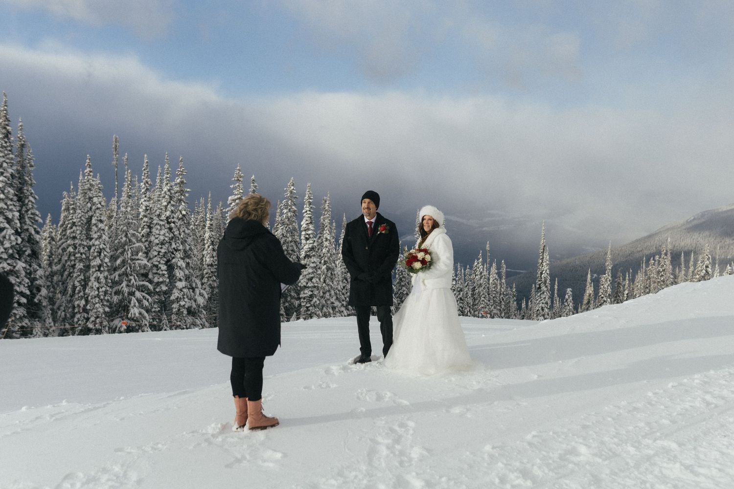 bride and groom smile at the officiant during their Revelstoke elopement on the snowy ski hill