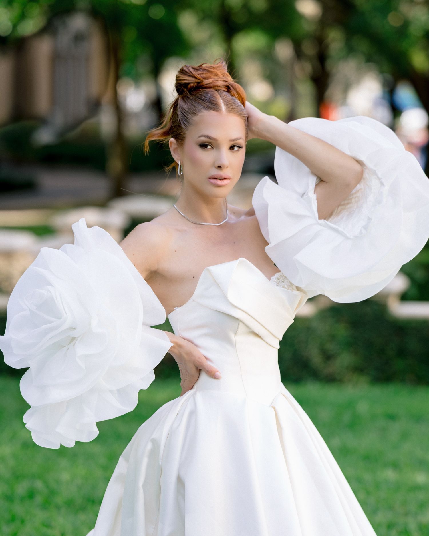 Bride in white strapless gown with dramatic ruffled sleeves poses outdoors on green lawn.