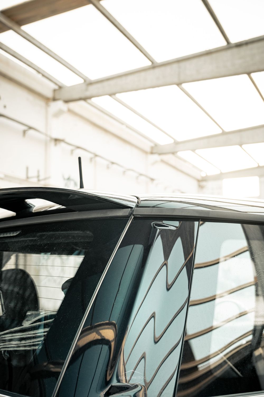 Close-up of a dark car roof and windows reflecting light inside a bright automotive garage with skylights.