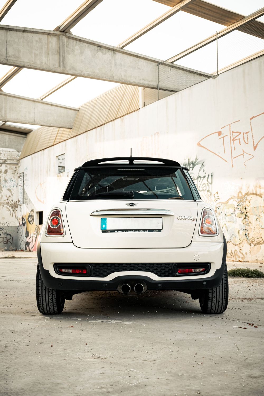 Rear view of a white Mini Cooper parked in an urban garage with graffiti walls and industrial ceiling.