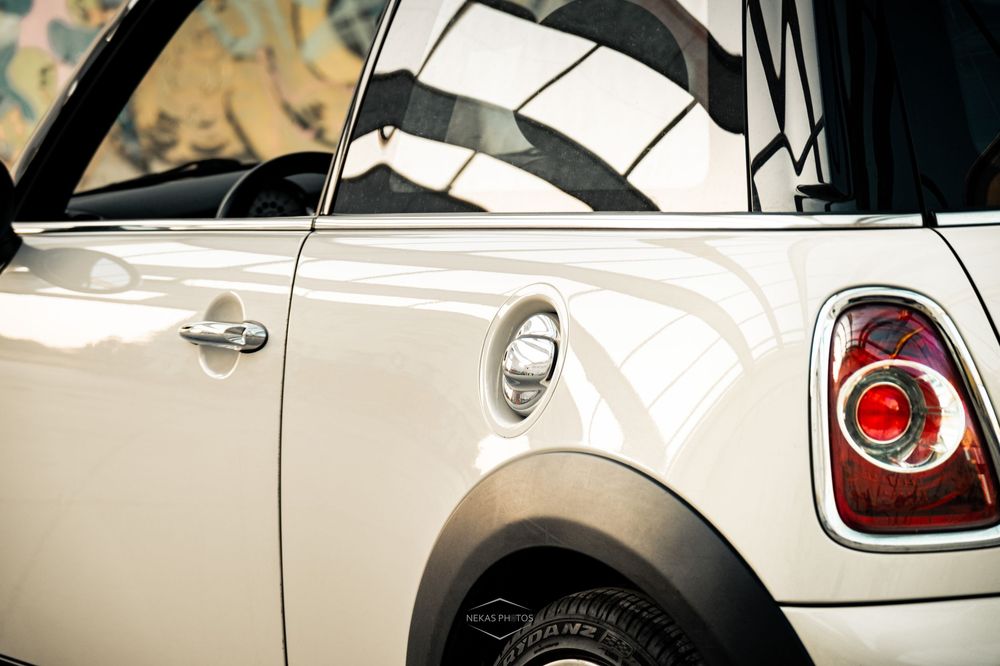 Close-up of a white Mini Cooper showing rear tail light, fuel cap, and black wheel arch detail.