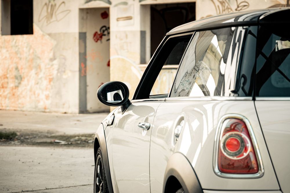 White Mini Cooper parked near a graffiti-covered building, showcasing its rear tail light and side mirror.