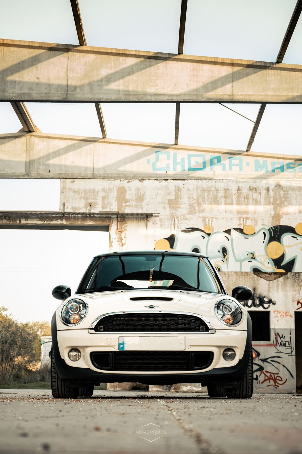 White Mini Cooper S parked in an abandoned building with graffiti walls, front view, urban photography.