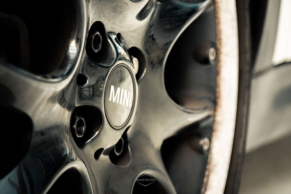 Close-up of a MINI Cooper alloy wheel hub cap with chrome spokes and dark metallic finish.