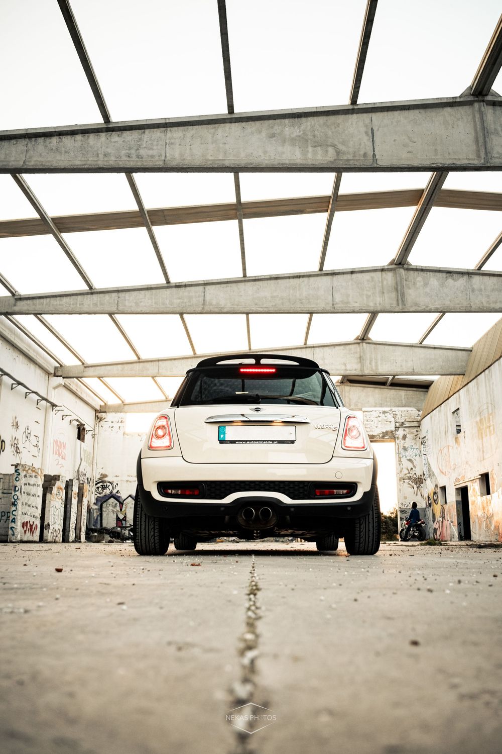 White MINI Cooper viewed from rear inside an abandoned building with graffiti walls and steel roof structure.