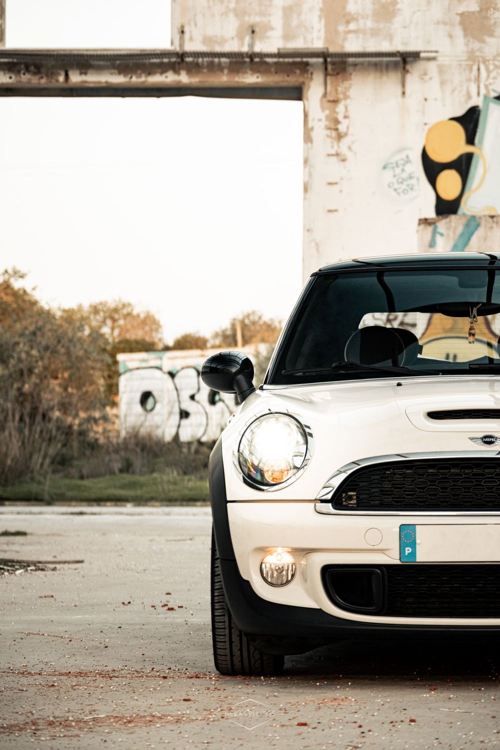 White Mini Cooper parked in front of an abandoned building with graffiti art on the wall.