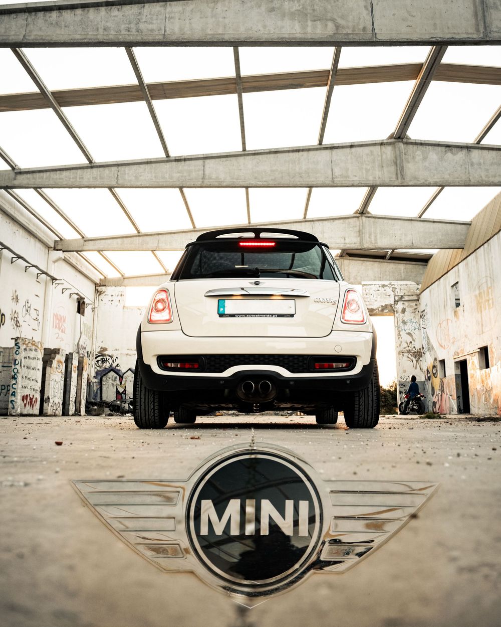 White MINI Cooper photographed from rear inside abandoned building with MINI logo reflected on ground.