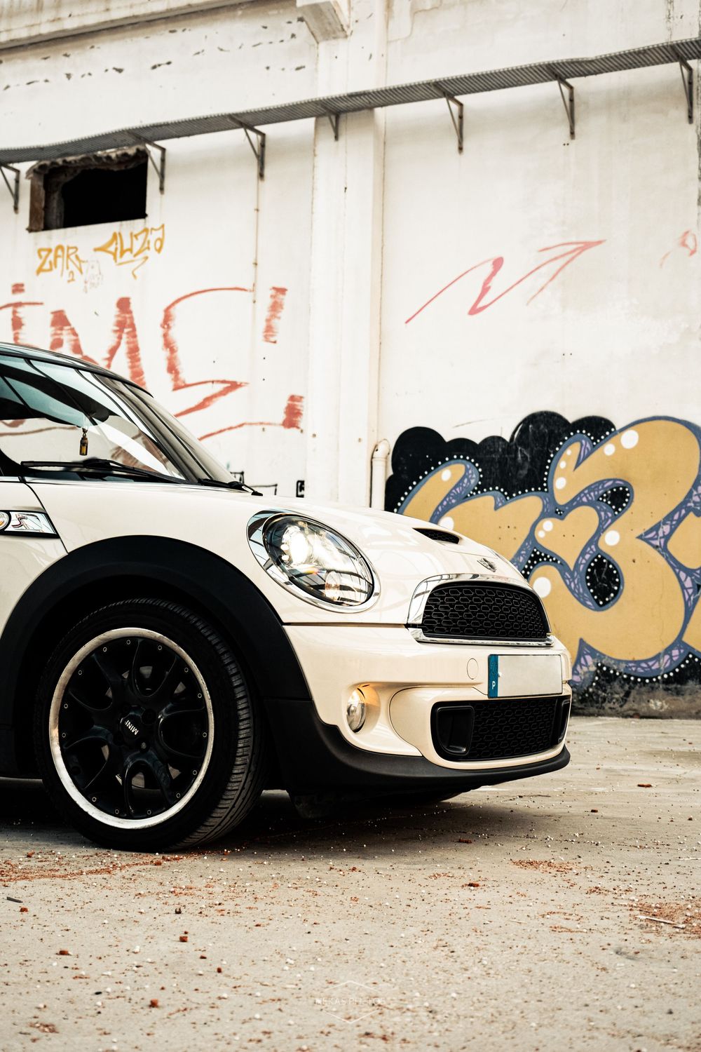 White Mini Cooper parked against a graffiti-covered wall in an urban setting.