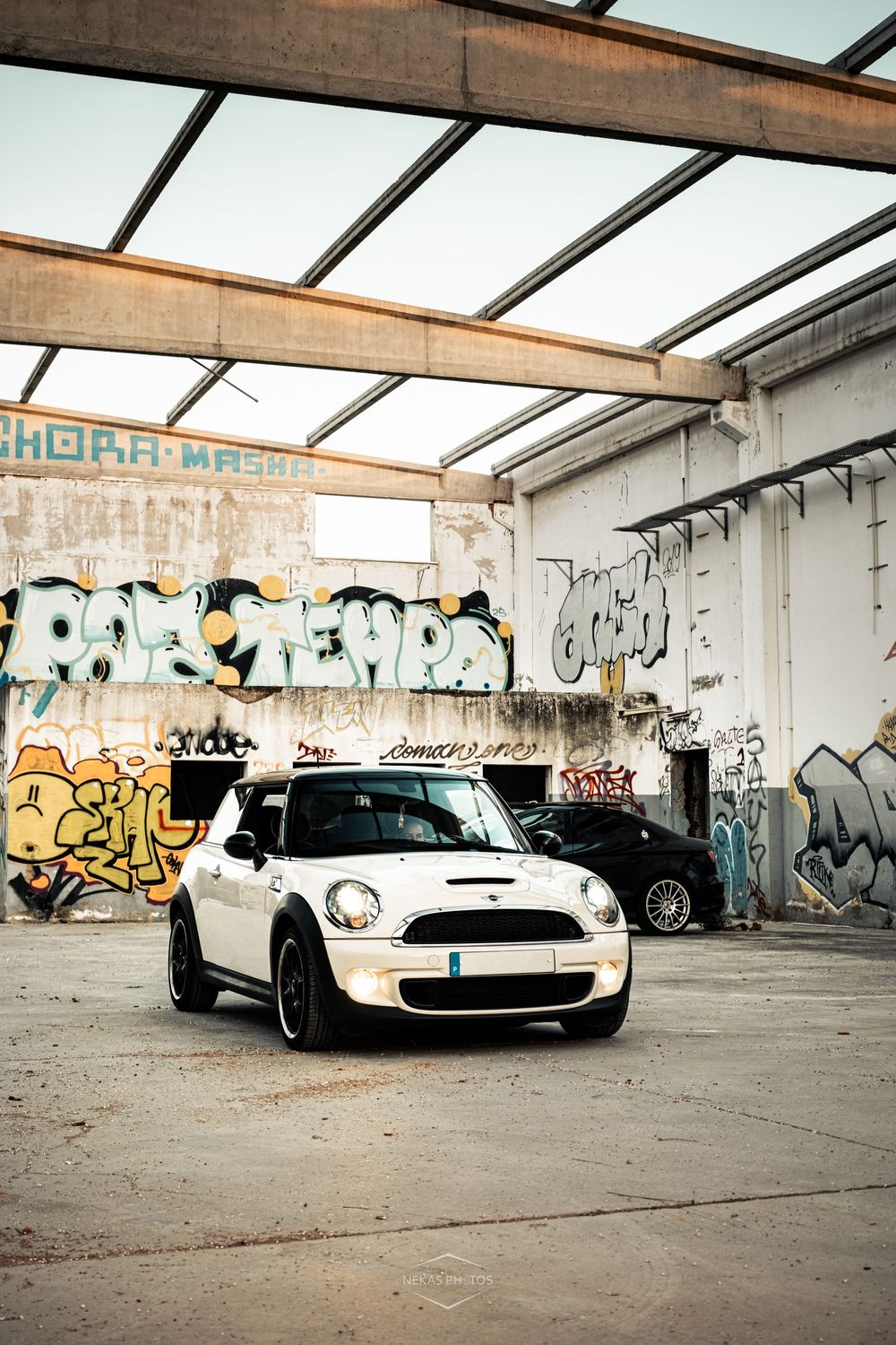 White Mini Cooper parked in an abandoned warehouse with colorful graffiti-covered walls and industrial ceiling.