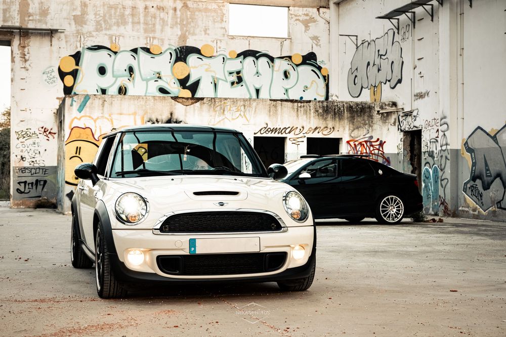 White Mini Cooper parked in front of a graffiti-covered building with a black car in the background.