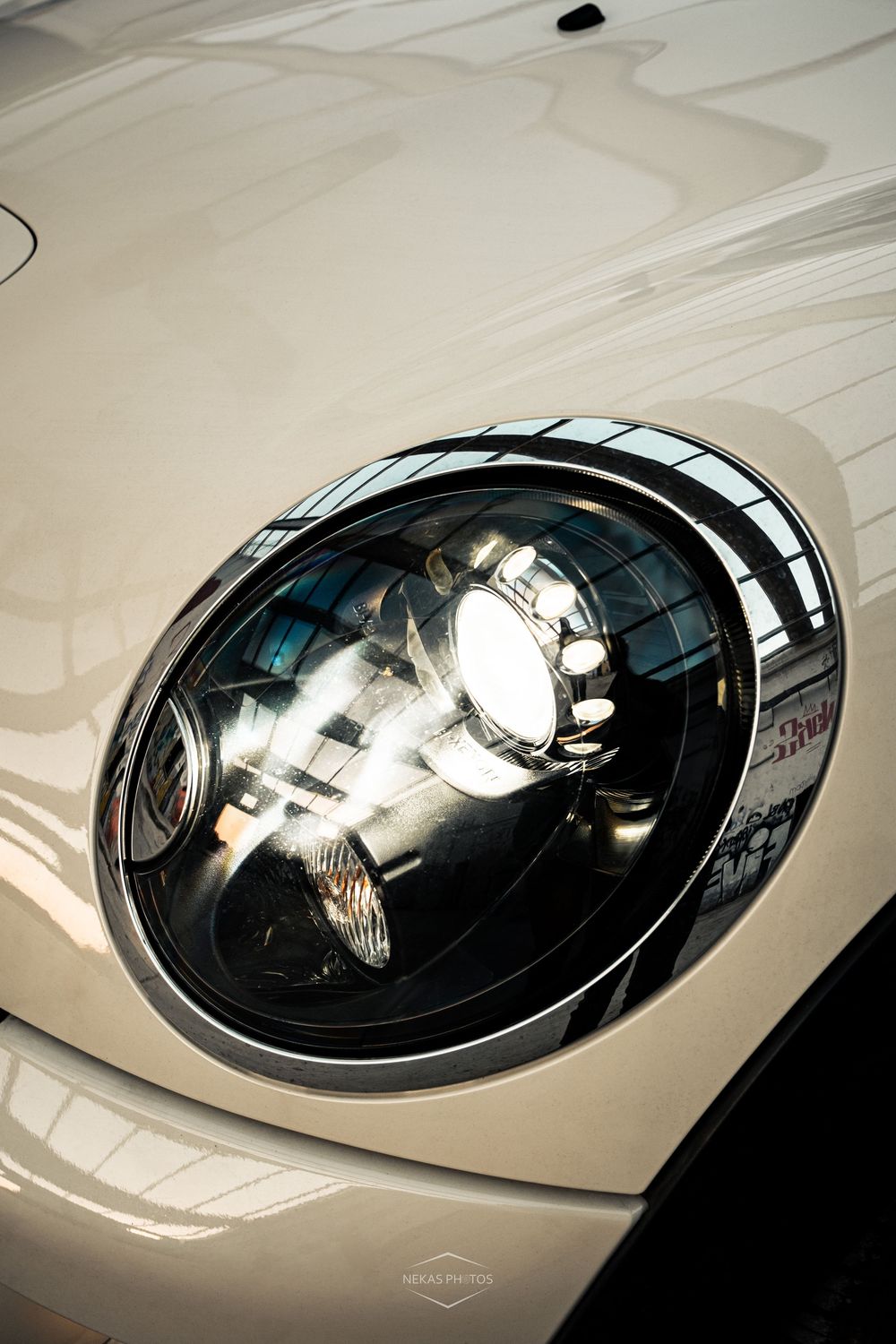 Close-up of a shiny round headlight on a white Mini Cooper car.