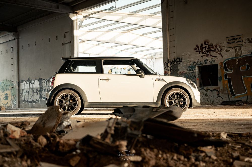 White Mini Cooper parked in an abandoned graffiti-covered building with debris on the ground.