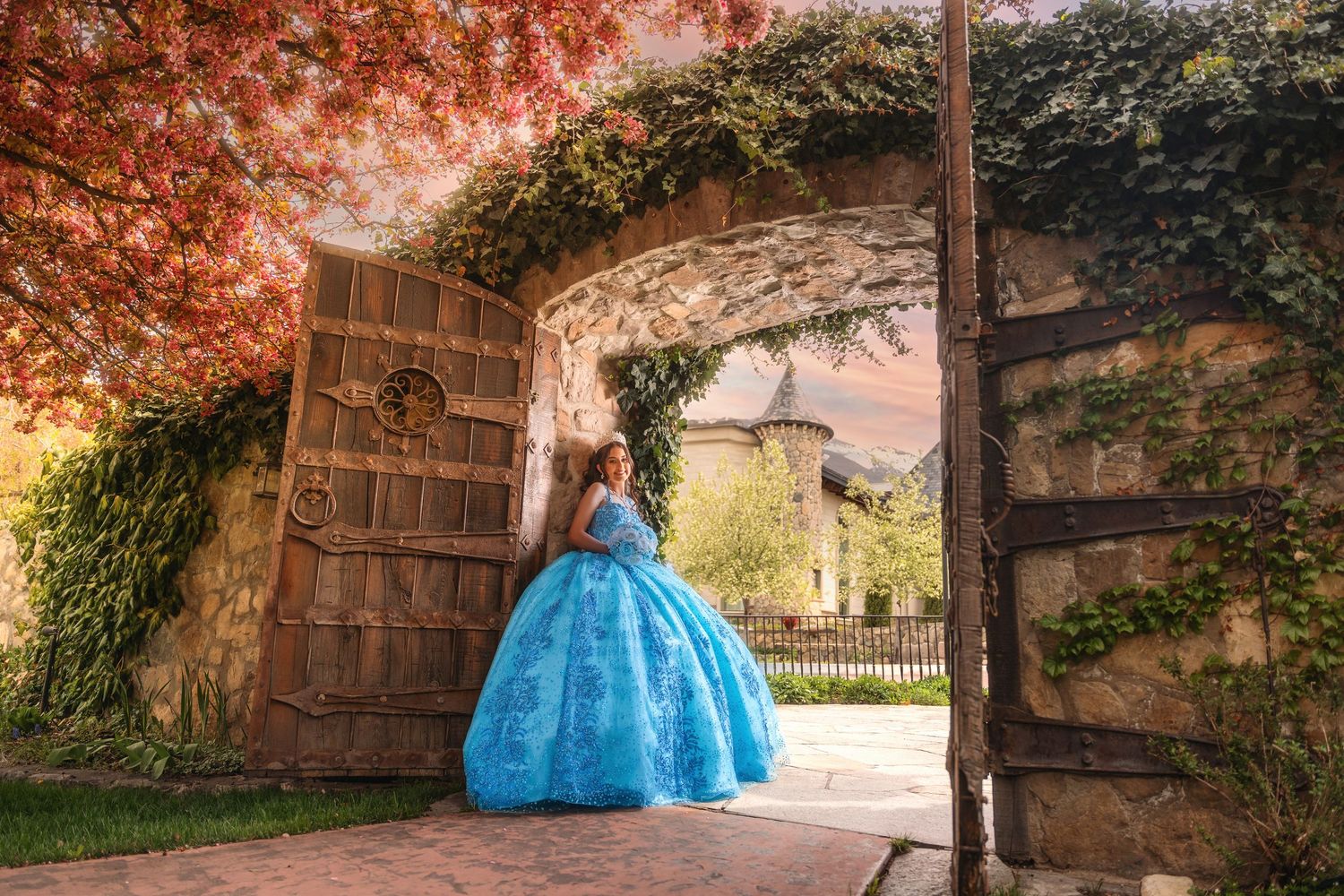 Young woman in a blue ball gown quinceañera dress poses under a stone arch with autumn foliage.