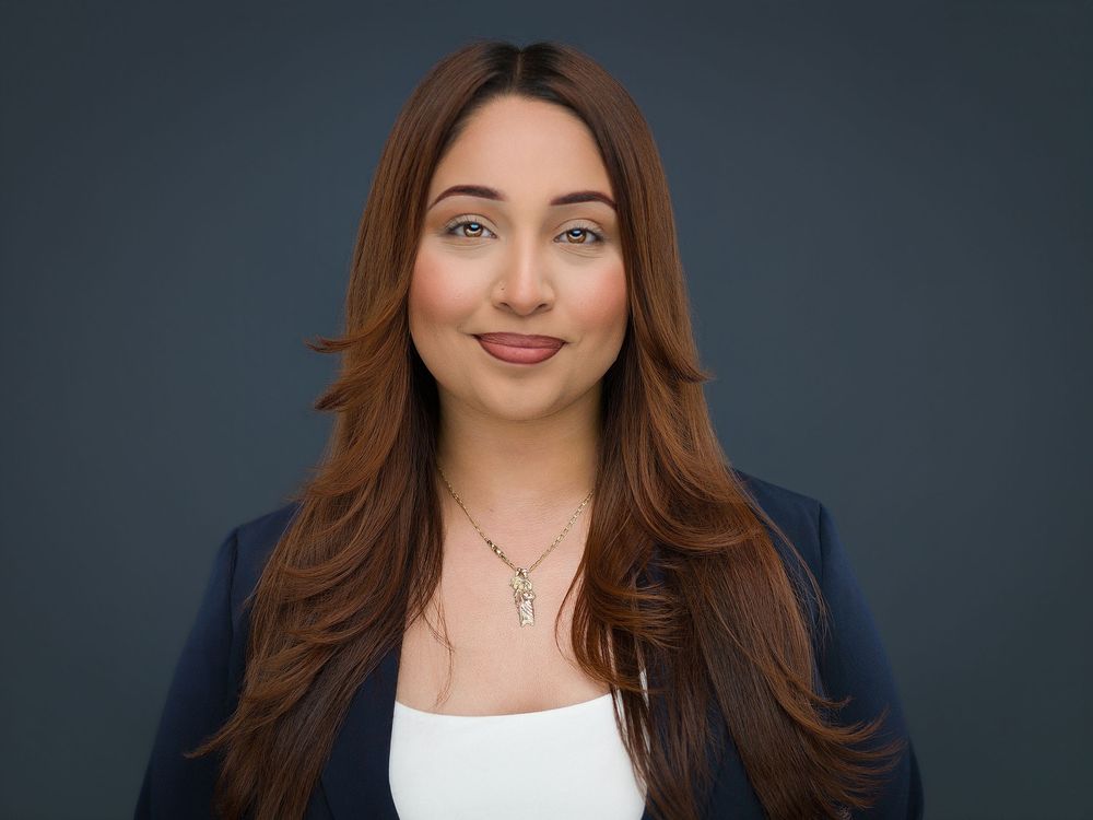 Professional headshot of a young woman with long auburn hair wearing a navy blazer and white top with a delicate necklace.