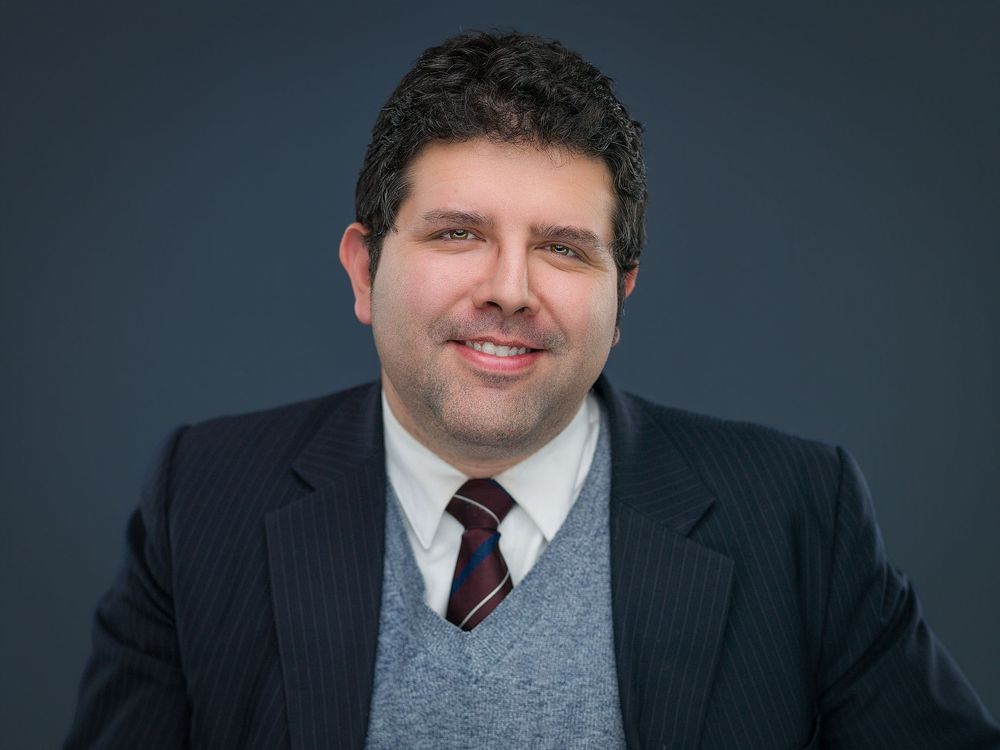 Professional businessman in a suit and tie smiling confidently against a dark gray background.
