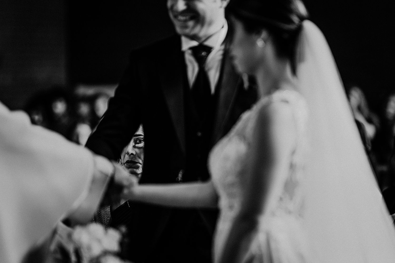Black and white photo of bride and groom holding hands during intimate wedding ceremony moment.