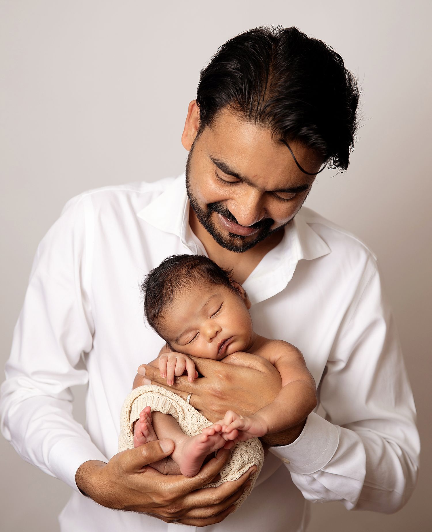 Black and white photo of adult hands touching a small baby hand, symbolising family love and connection. During a newborn session in London