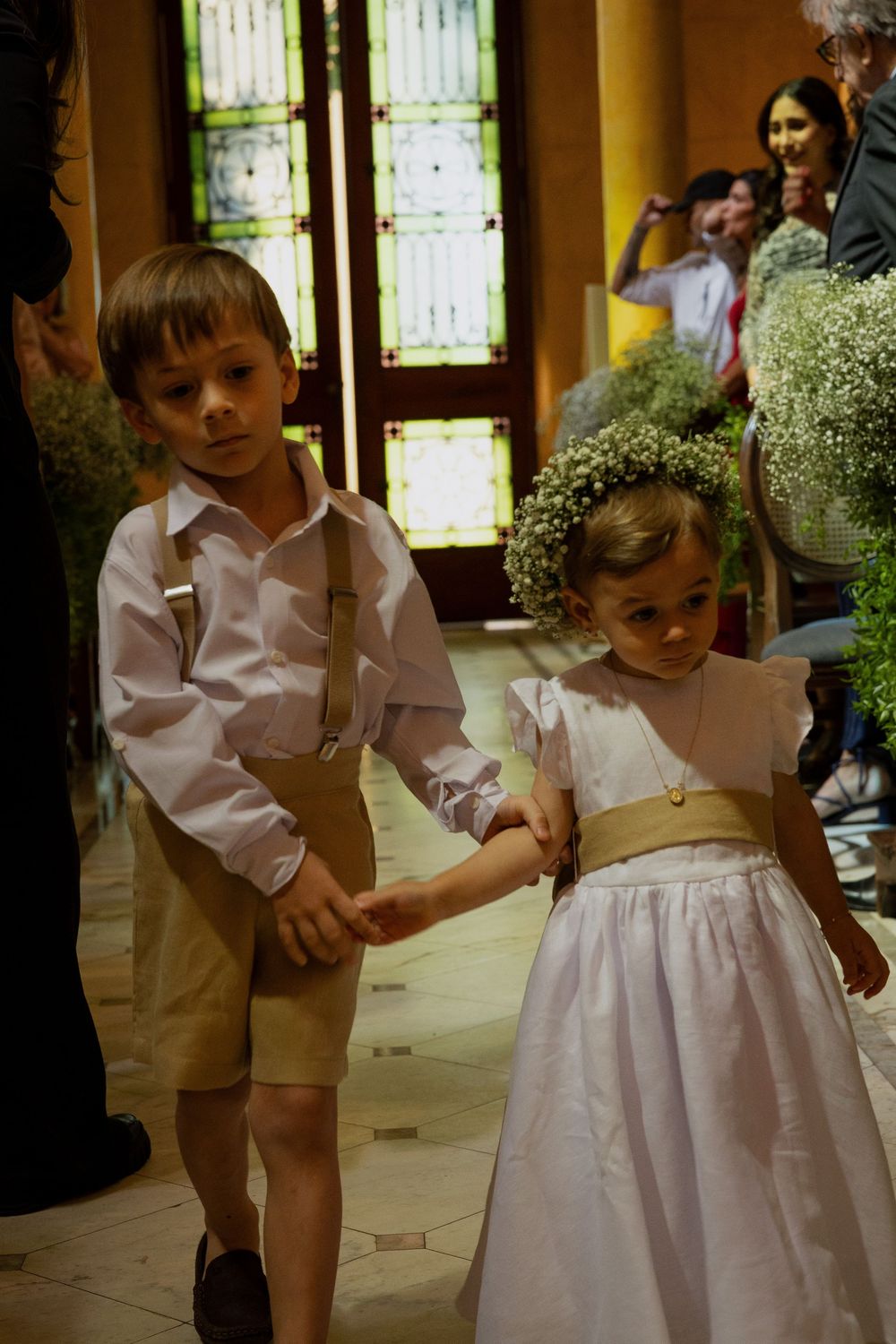 Ring bearer and flower girl walking down the aisle at a wedding ceremony, dressed in formal attire.