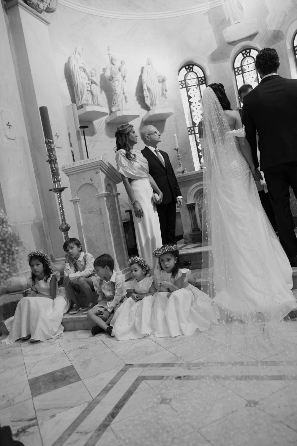 Black and white photo of a wedding ceremony in a church with flower girls seated on steps near the altar.