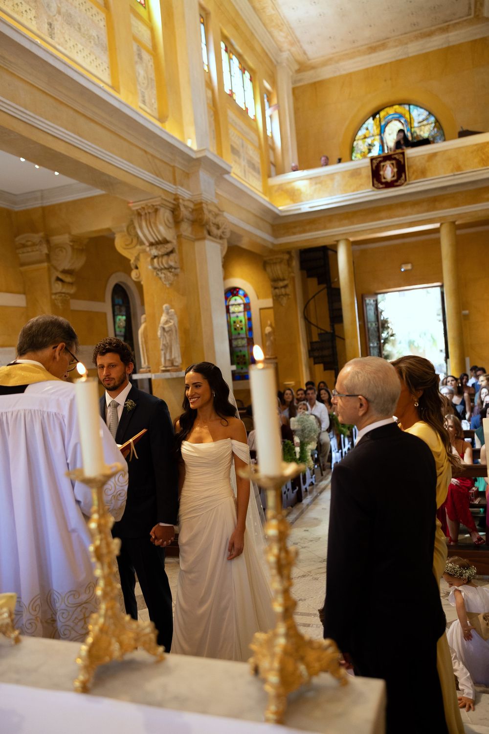 Elegant wedding ceremony in a golden church with bride and groom holding hands at the altar.