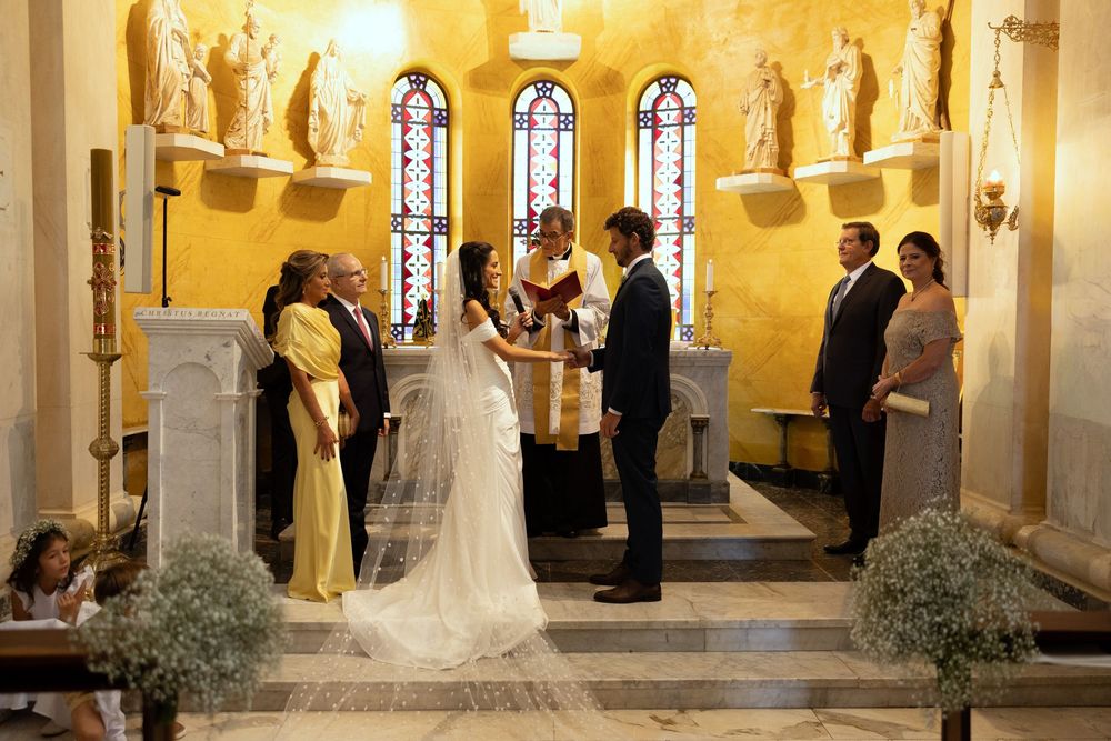A wedding ceremony inside a historic church with a bride in white gown and veil exchanging vows before a priest.