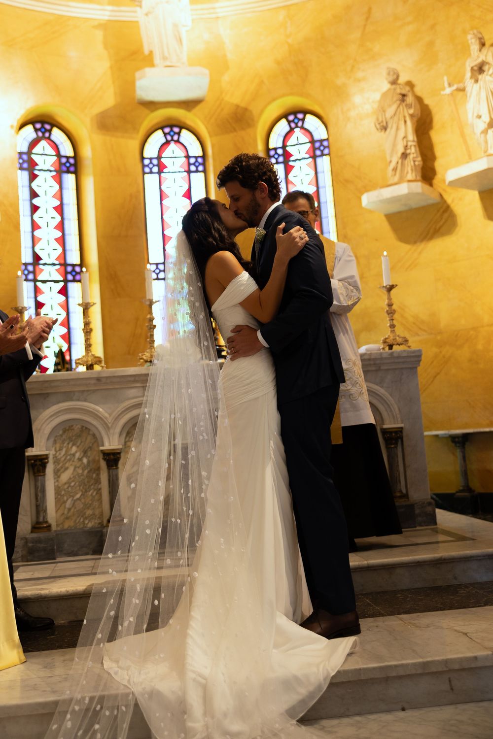 Bride and groom share their first kiss at the altar during a romantic church wedding ceremony with stained glass windows.
