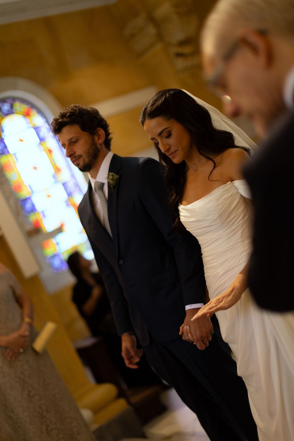 Bride and groom holding hands with bowed heads during solemn wedding ceremony prayer in church.