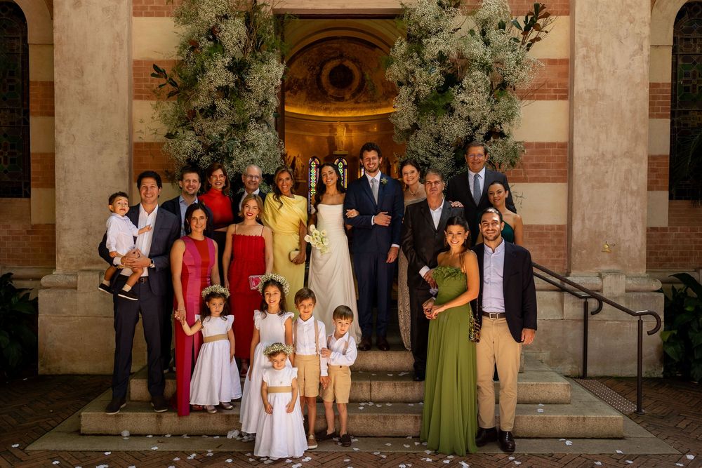 Large family group photo at a wedding ceremony on church steps, with bride and groom in center surrounded by guests.