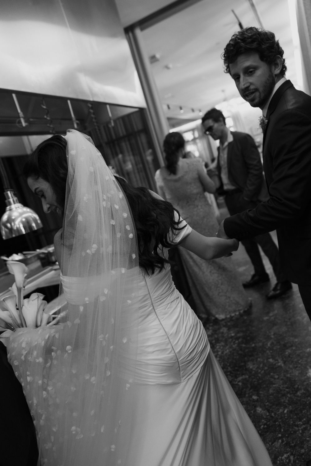 Black and white wedding photo of bride in veil and gown dancing with groom in suit at elegant reception.