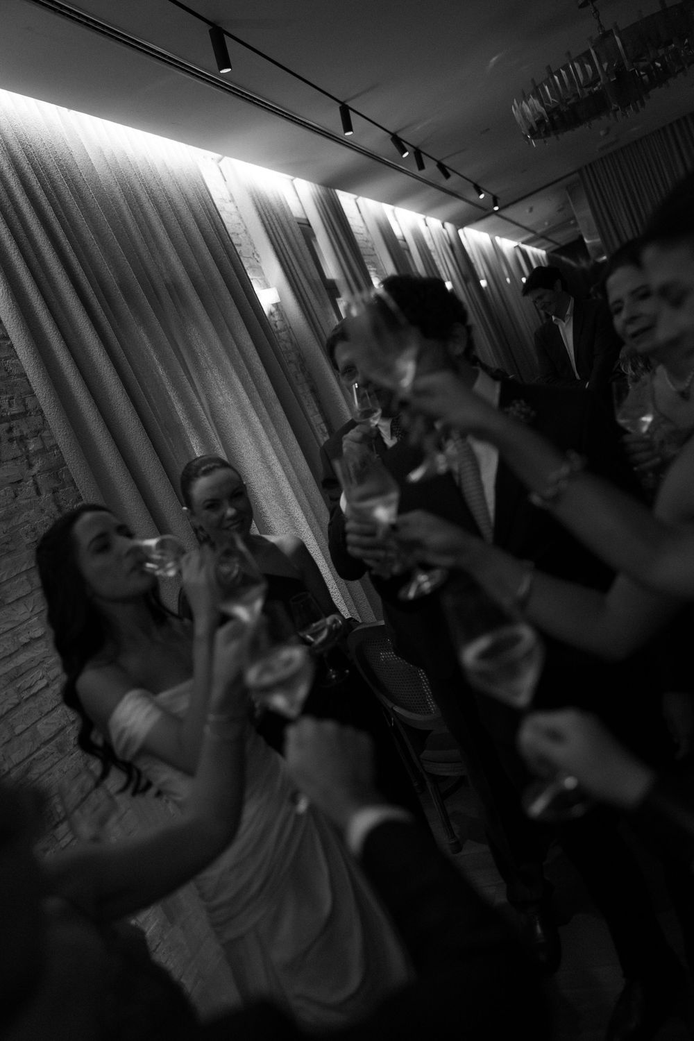 Black and white photo of elegantly dressed guests raising glasses in a toast at a formal wedding reception.