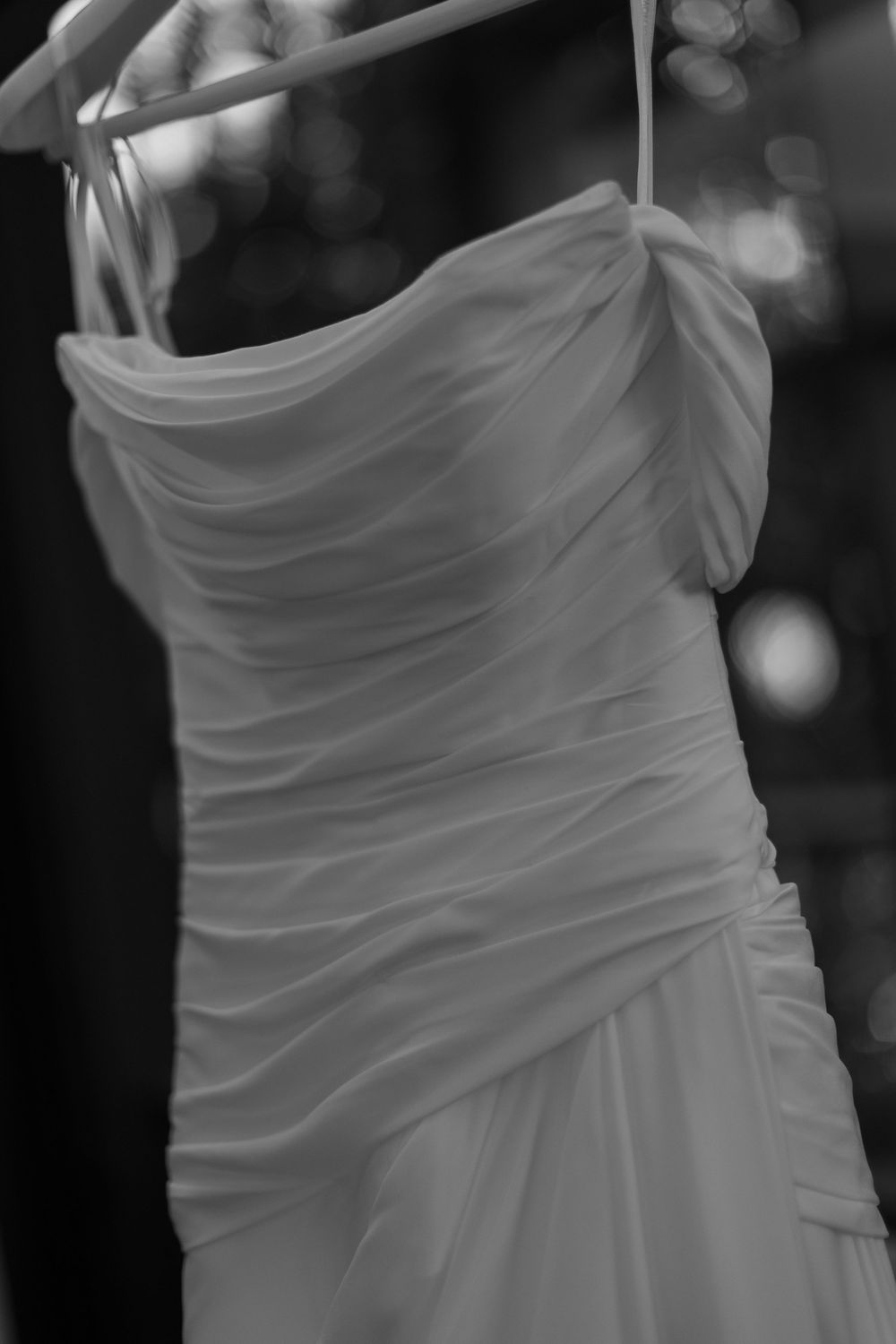 Black and white photo of an elegant ruched wedding gown with spaghetti straps hanging on a hanger.
