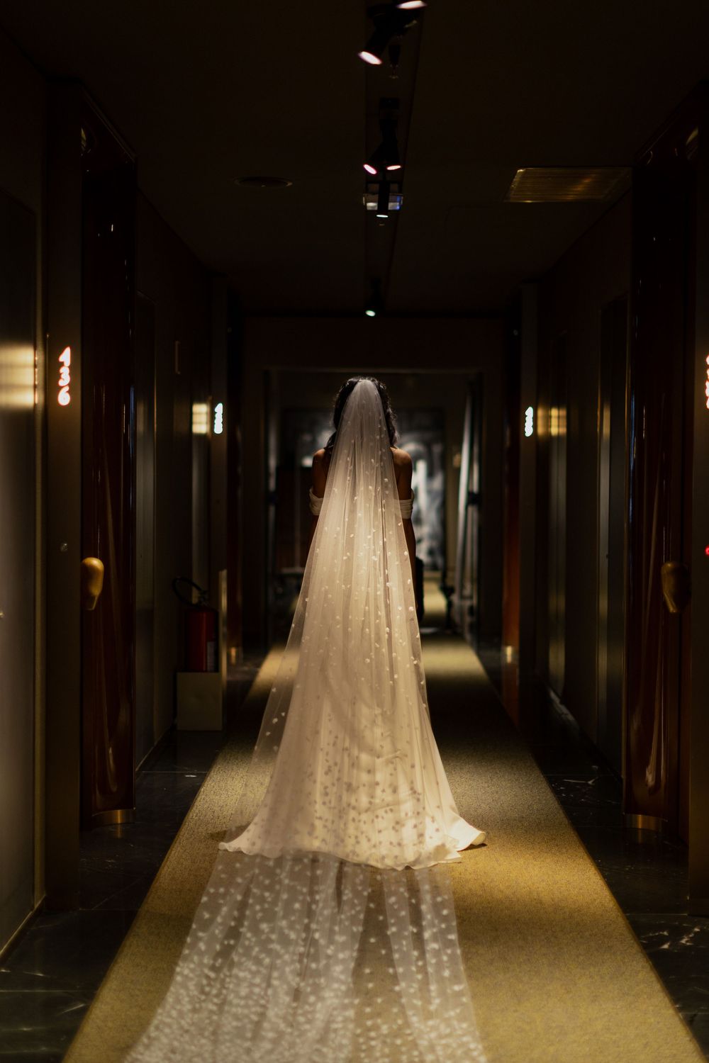 Elegant wedding veil displayed in a dimly lit hotel corridor, trailing on the floor with delicate floral details.