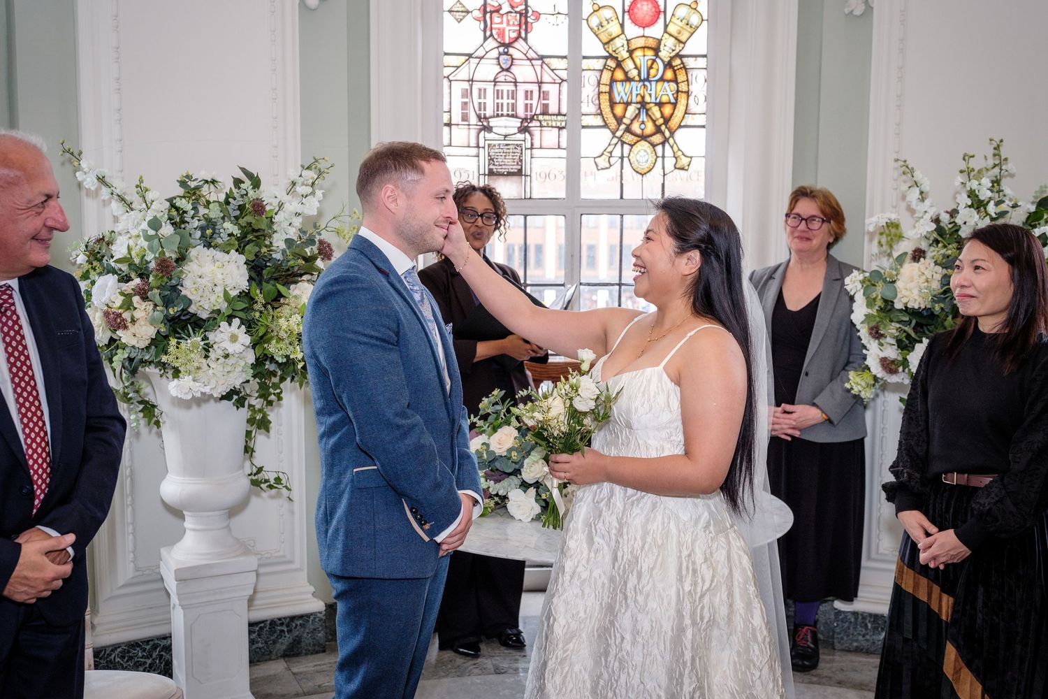 A wedding party celebrating, with a bride and groom embracing while guests applaud in the background.