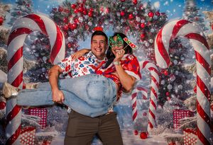 Couple posing playfully in front of festive Christmas backdrop with candy canes and decorated trees.