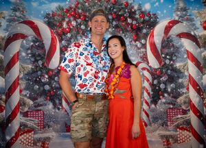 Couple posing in front of festive Christmas backdrop with candy canes and ornaments at holiday party.