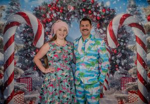 Couple posing in festive tropical Christmas outfits in front of a holiday backdrop with candy canes and ornaments.