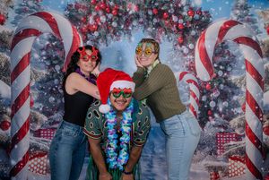Three friends wearing fun Christmas accessories pose in front of holiday candy cane backdrop.