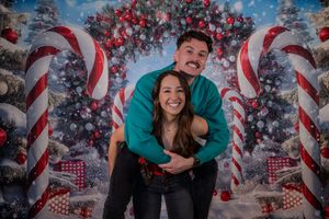 Couple embracing in front of festive Christmas backdrop with candy canes and decorated trees.
