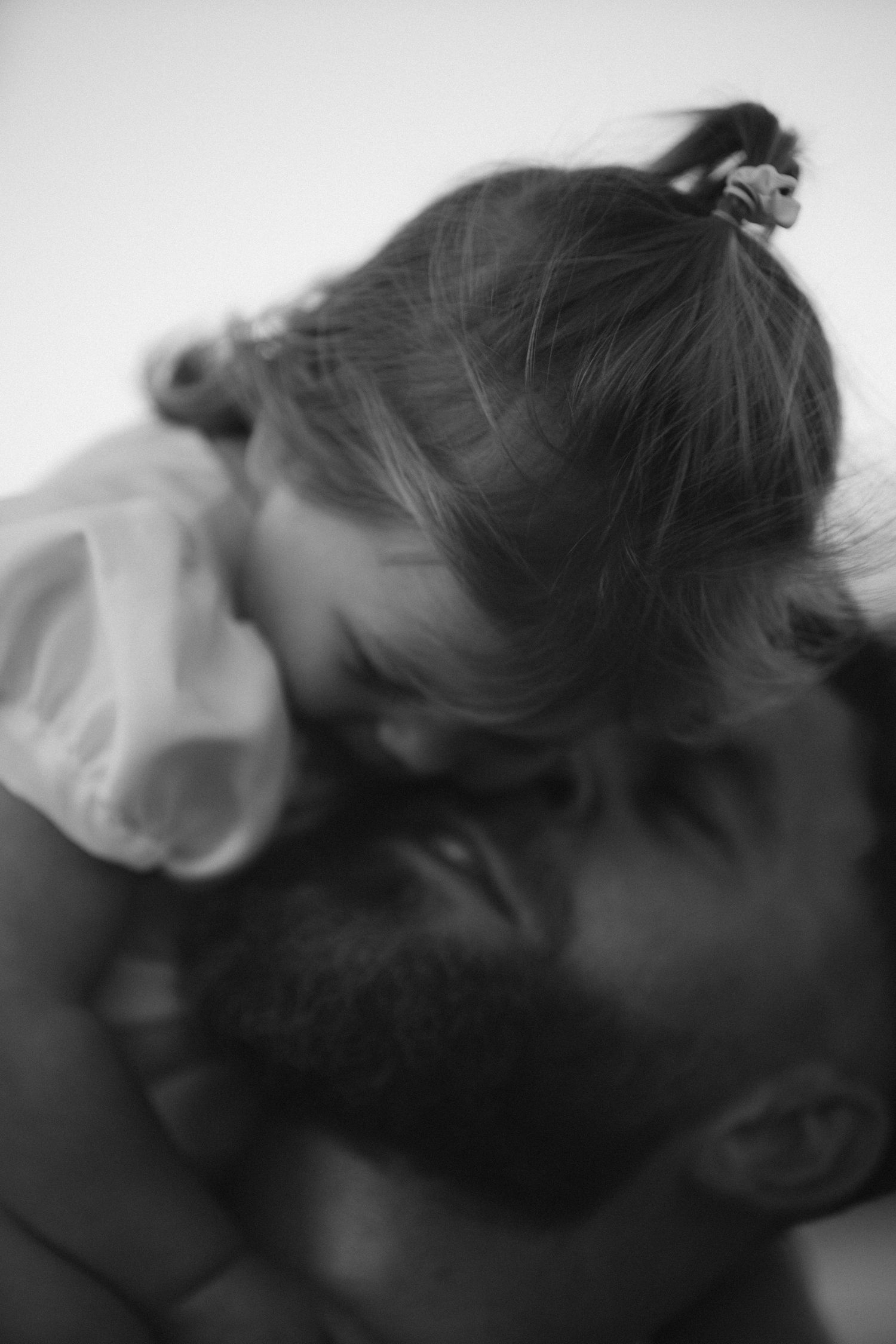 Black and white photo of a bearded father tenderly embracing his young daughter with a ponytail.